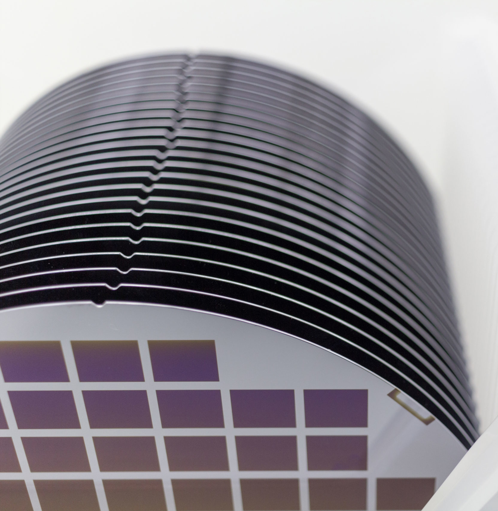 Silicon Wafers in white plastic holder box on table ,background is white color- A wafer is a thin slice of semiconductor material, such as a crystalline silicon, used in electronics for the fabrication of integrated circuits.Wafers with microchips.Rainbow on silicon wafers.Color silicon wafers with glare.